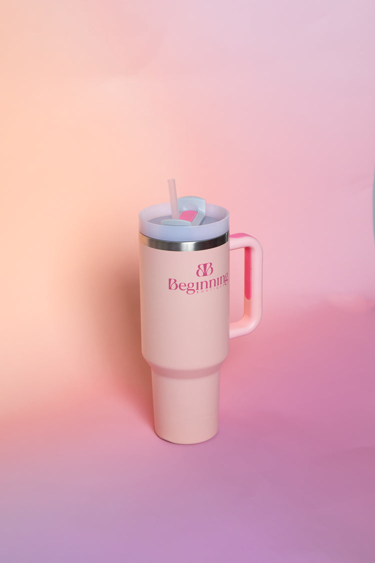 Front view of a light pink tumbler with a handle, light blue lid, pink straw, and pink logo