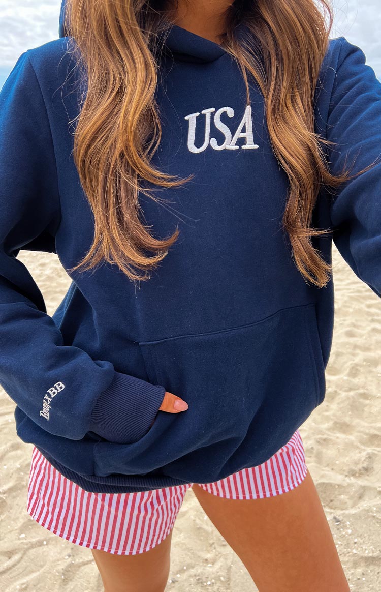 Close-up of the navy hoodie showing white USA embroidery, kangaroo pocket, and white BB logo on the ribbed cuff
