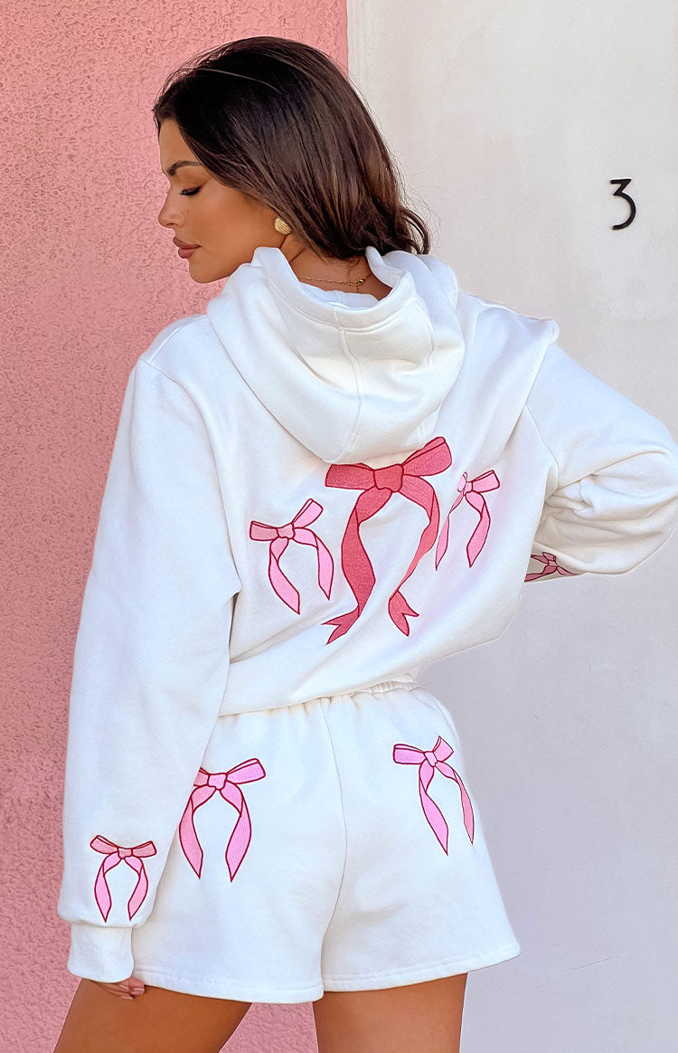 Girl is wearing a white hoodie set with pink bows embroidered on the back.