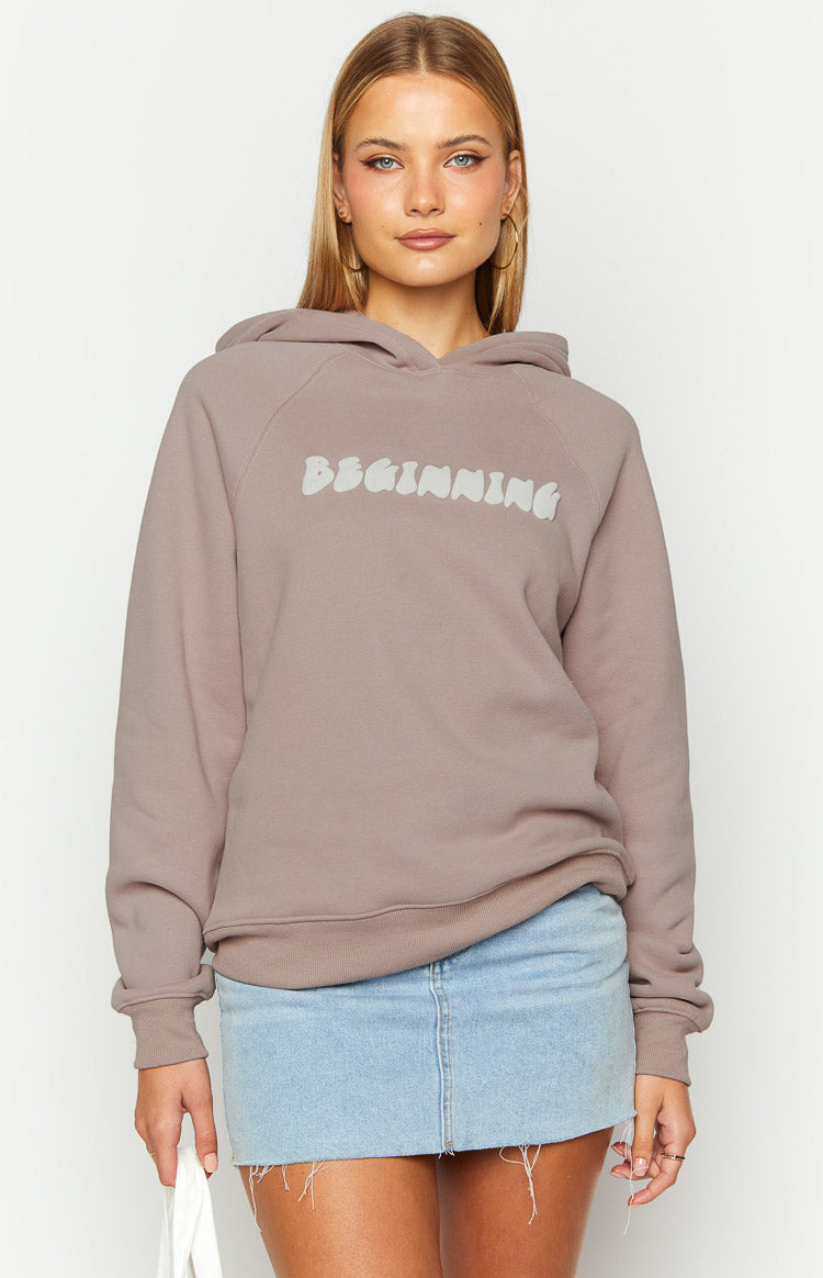 Front view of a beige hoodie with "BEGINNING" in a white bubble font on the chest, raglan sleeves and ribbed cuffs