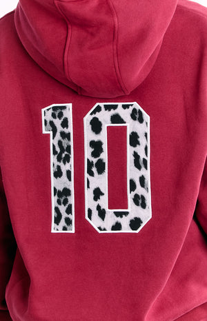 The back of a red hooded sweatshirt featuring a large number 10 applique with a black and white cow print pattern.
