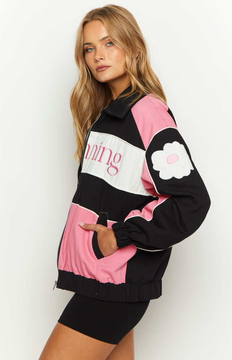 Side view of a black, pink, and white color block bomber jacket with a white flower patch on the sleeve and side pocket