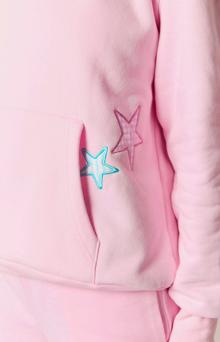 Close-up of the pink hoodie's kangaroo pocket, featuring a light blue striped star and a pink gingham star patch