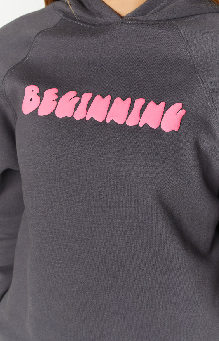 Close-up of the pink bubble text 'BEGINNING' graphic on the slate grey hoodie