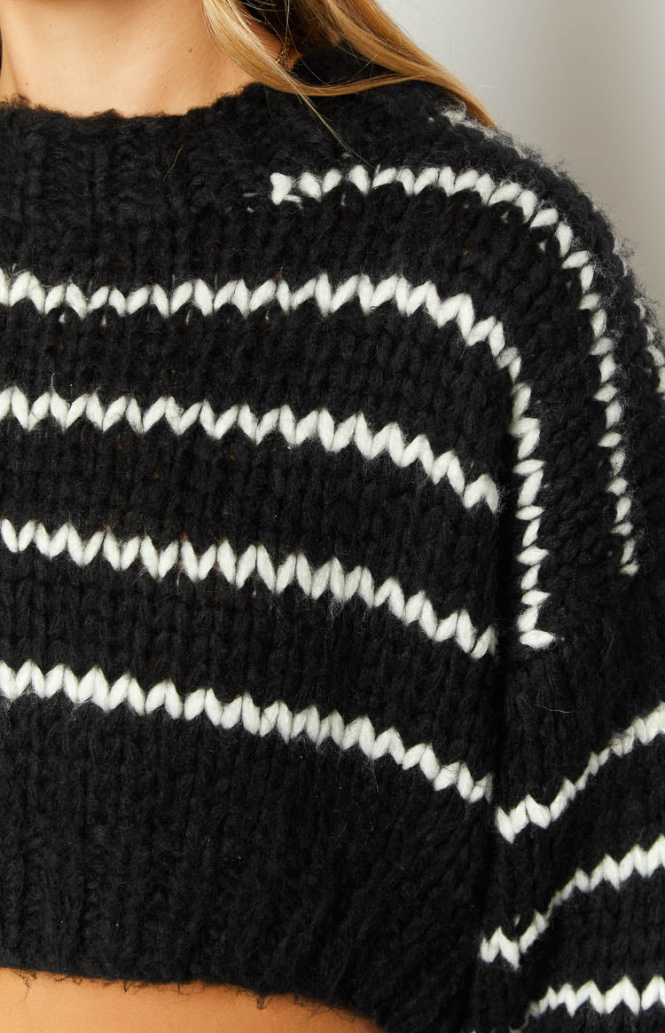 Close-up of the black and white striped sweater, highlighting the thick knit texture and zigzag white stripes