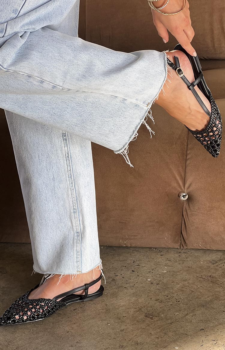Close-up of the black woven mules with a pointed toe and slingback strap being adjusted