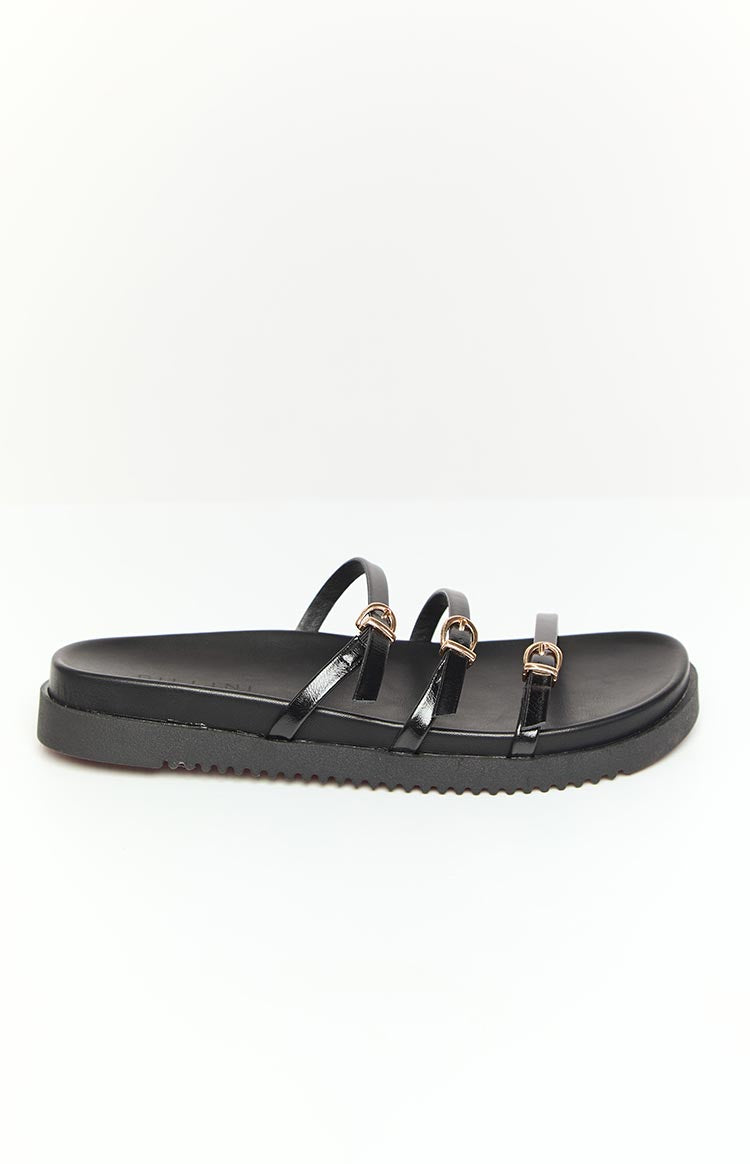 Side view of a black slide sandal with three glossy straps and gold D-ring buckles on a thick ridged sole