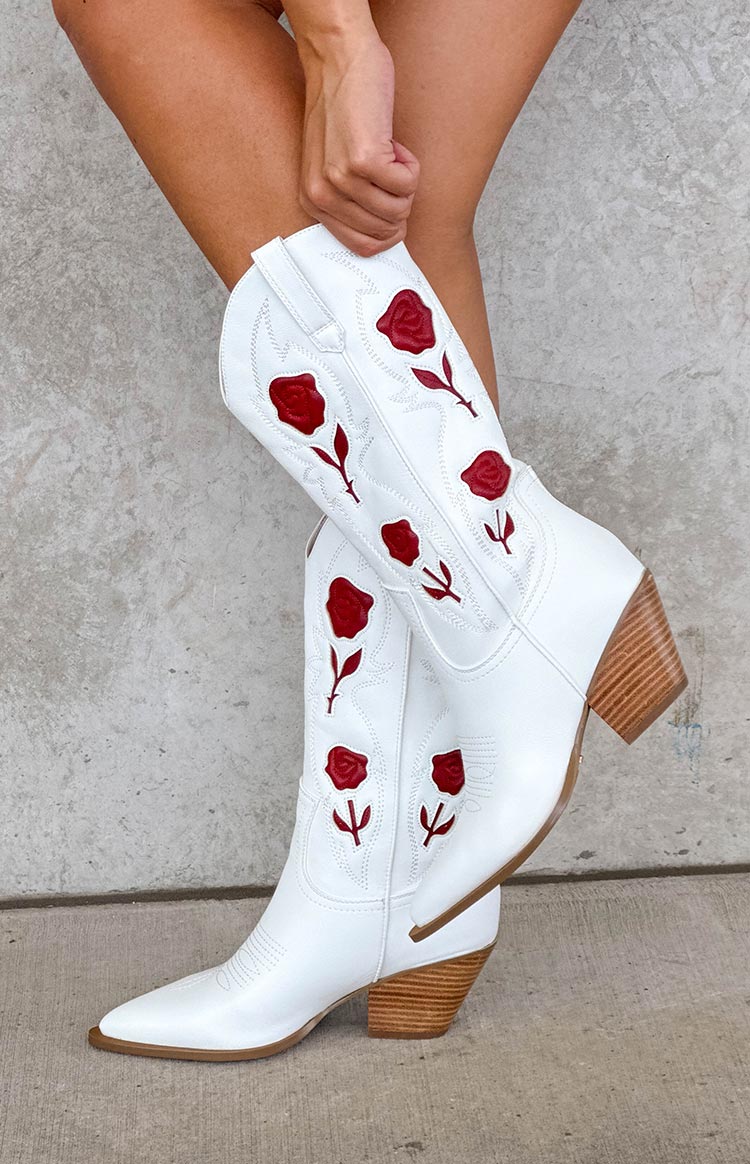 Side view of white cowboy boots with red rose embroidery, pointed toe, and stacked wooden heel