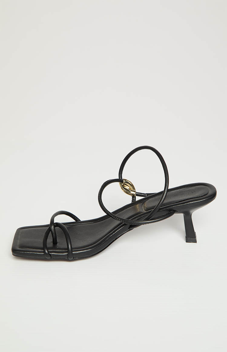 Side view of black square toe heels with thin straps and a gold ring detail on the ankle strap