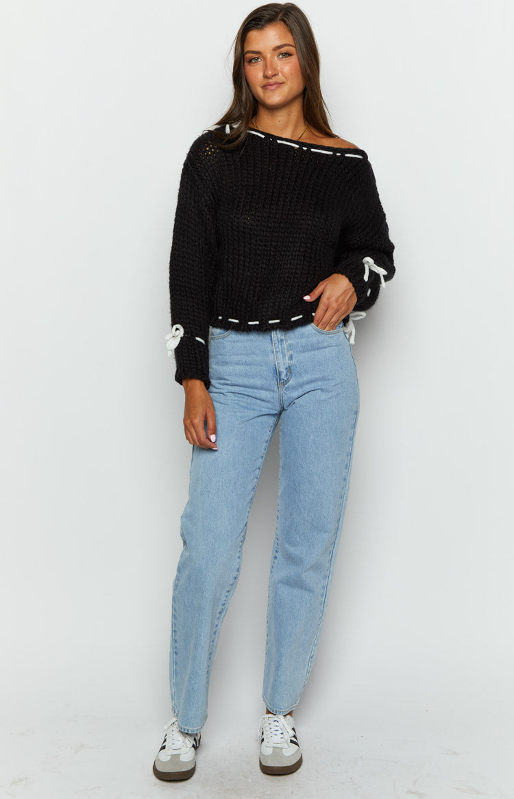 Black chunky knit sweater with white stitching detail along the off-shoulder neckline, hem, and cuffs with ties