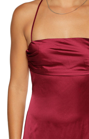 Close-up of the burgundy satin maxi dress showing the ruched strapless bodice and thin spaghetti strap