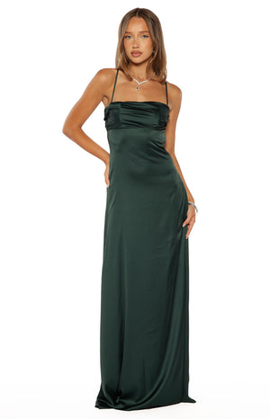 A full-length shot of our model wearing an emerald green satin maxi dress. This dress features thin spaghetti straps a square-cut bodice with subtle horizontal draping and a long flowing skirt.