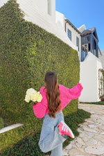Rear view of a bright pink chunky knit cardigan with an oversized fit and voluminous long sleeves