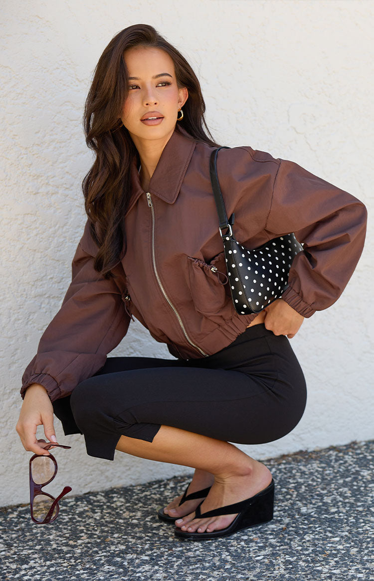 Side view of a chocolate brown cropped bomber jacket with drawstring front pockets and elasticated cuffs