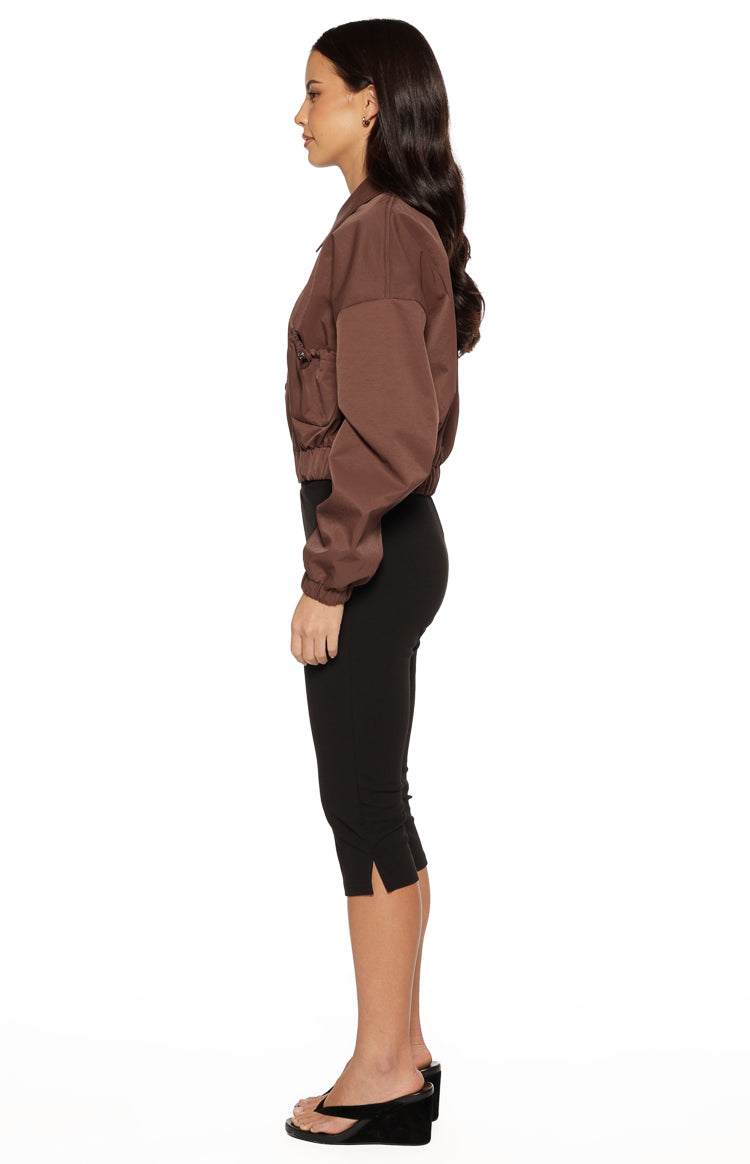 Side view of a chocolate cropped bomber jacket with a collar, voluminous long sleeves, and side drawstring detail
