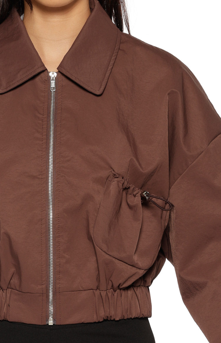 Close-up of the chocolate bomber jacket showing the drawstring detail on the front and elasticated hem