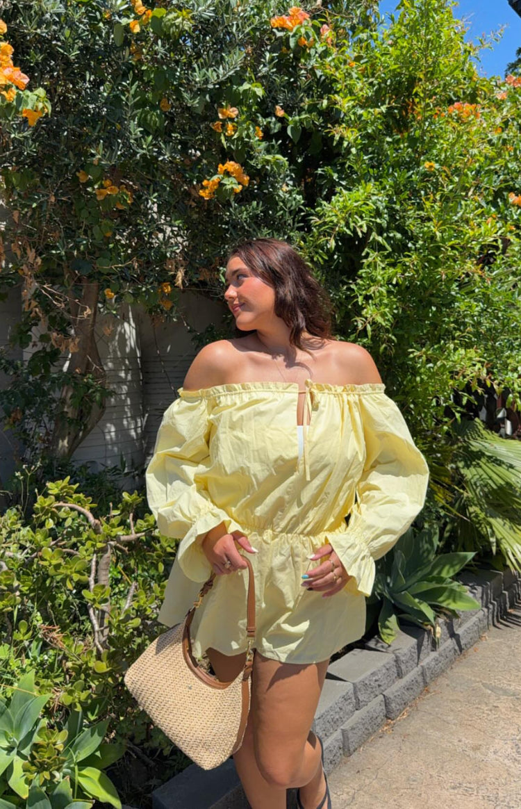 Side view of a yellow Bardot mini dress with long puff sleeves, elasticated waist, and front tie detail