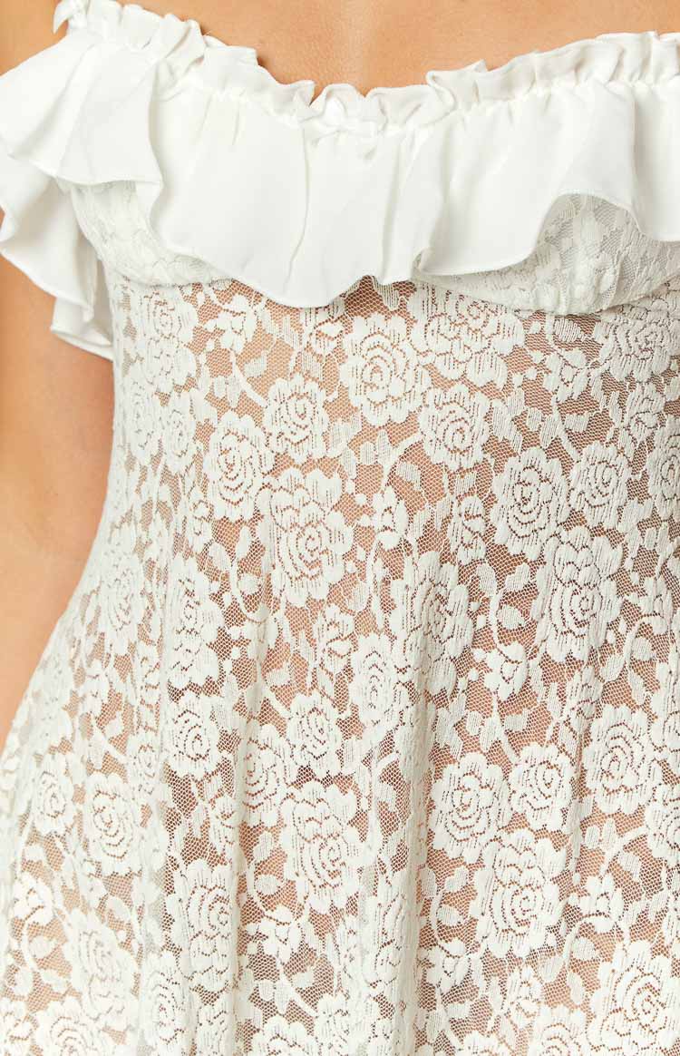 Close-up of the white floral lace fabric with its intricate pattern and the ruffled off-shoulder neckline