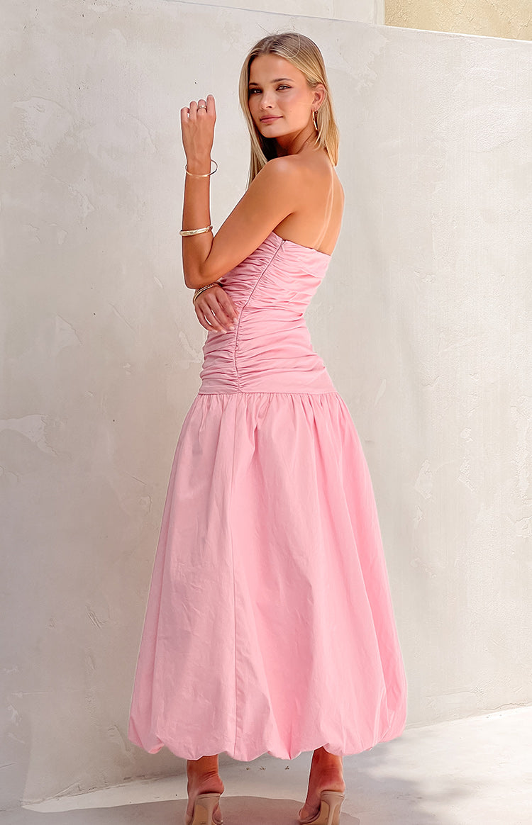 Side view of a pink strapless maxi dress with a ruched bodice and a full gathered skirt