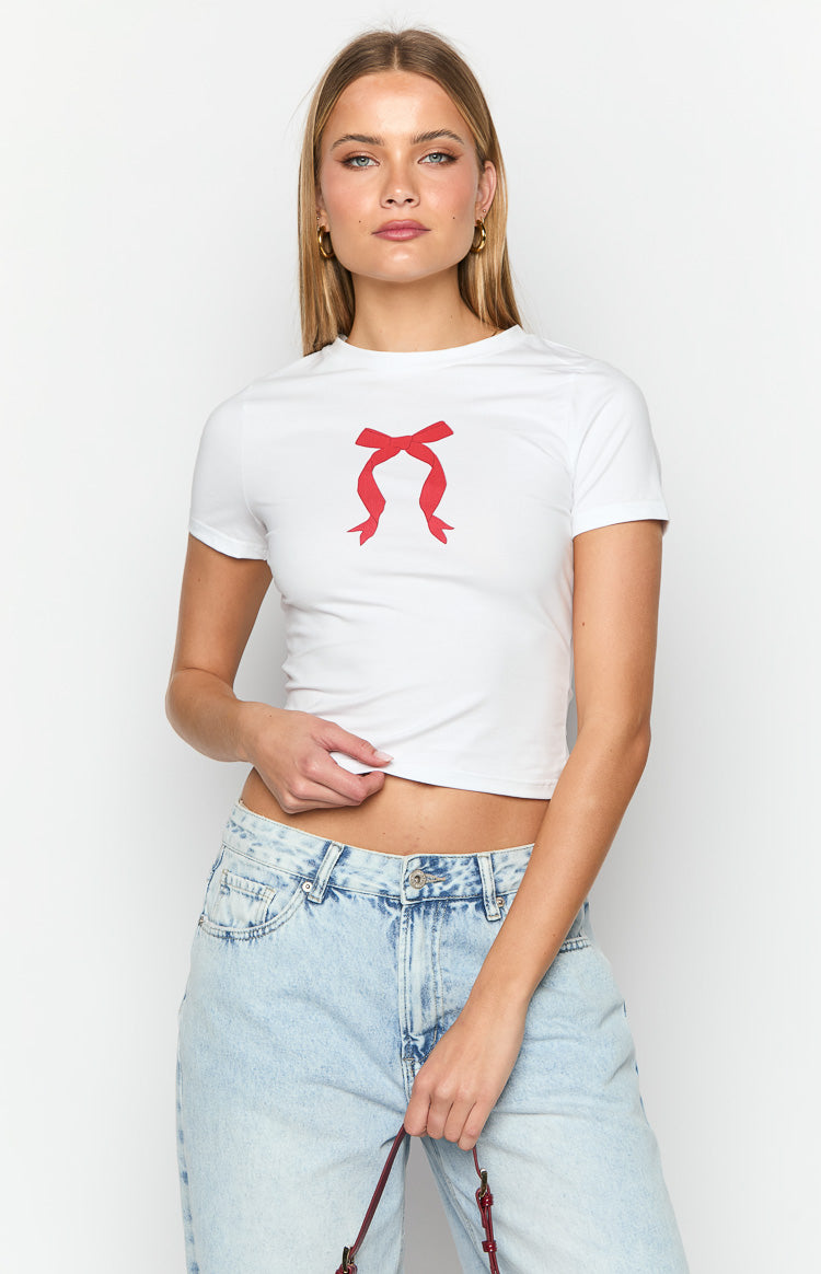 White fitted baby tee with a red bow graphic on the chest, crew neck, and short sleeves