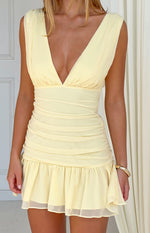 Close-up of the yellow ruched mini dress showing the deep V-neck and layered ruffled hem
