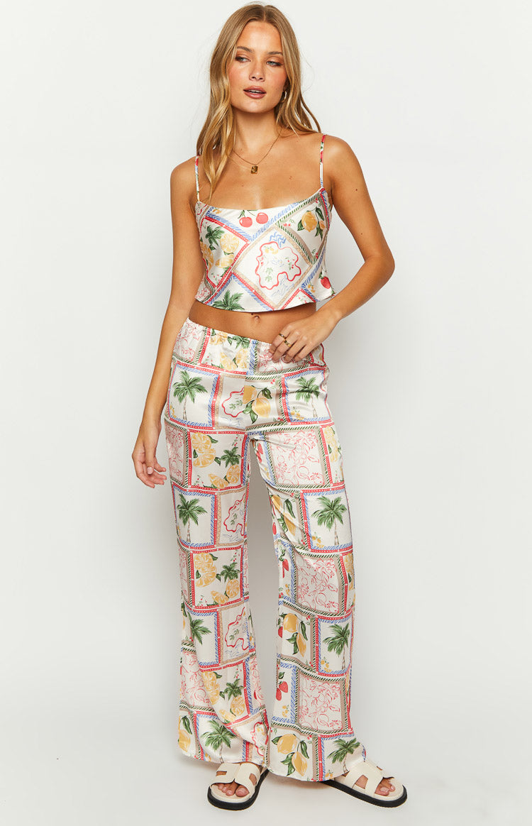 White satin wide-leg pants with a detailed patchwork print featuring lemons, cherries, and palm trees