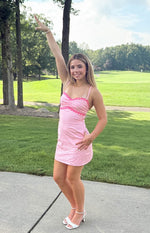 Side view of a pink fitted mini dress with sweetheart neckline, thin straps, and pink flower trim