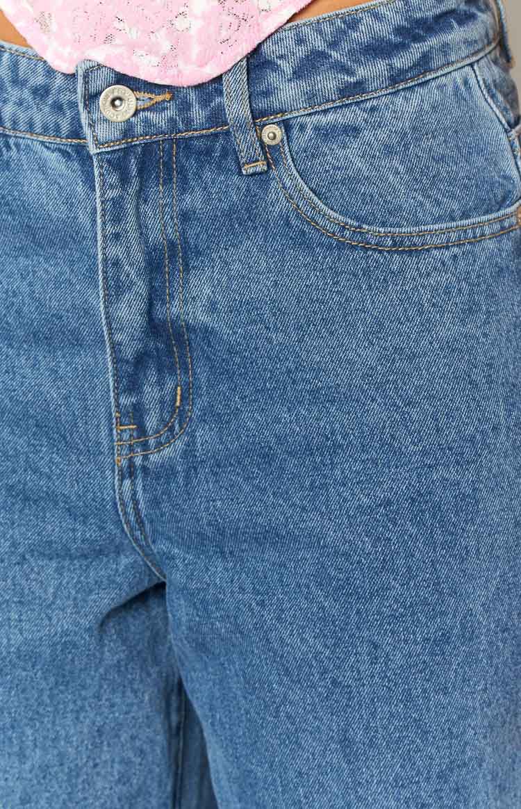 Close-up of the mid-wash blue denim jeans showing the front button closure, zipper fly, and coin pocket