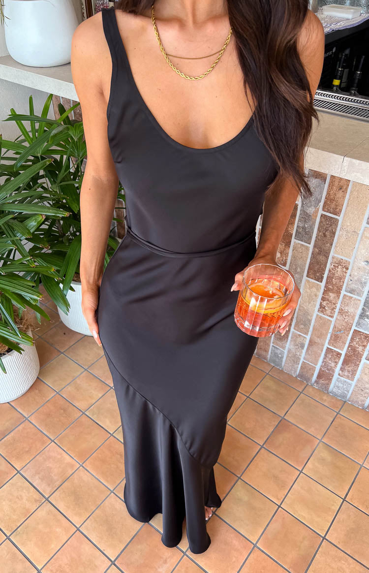 Angled view of the black satin maxi dress showing the fitted waist and diagonal seam creating a flared hem