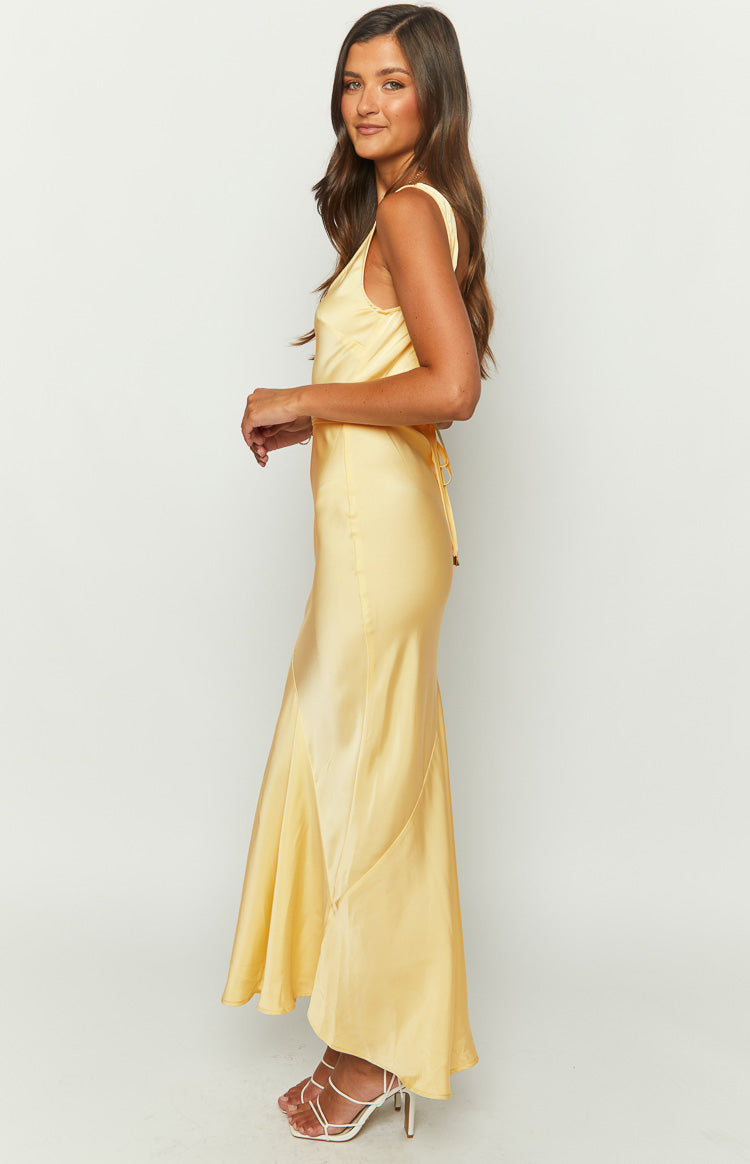 Side view of a carnation yellow satin maxi dress with a fitted bodice, flowing paneled skirt, and back tie detail