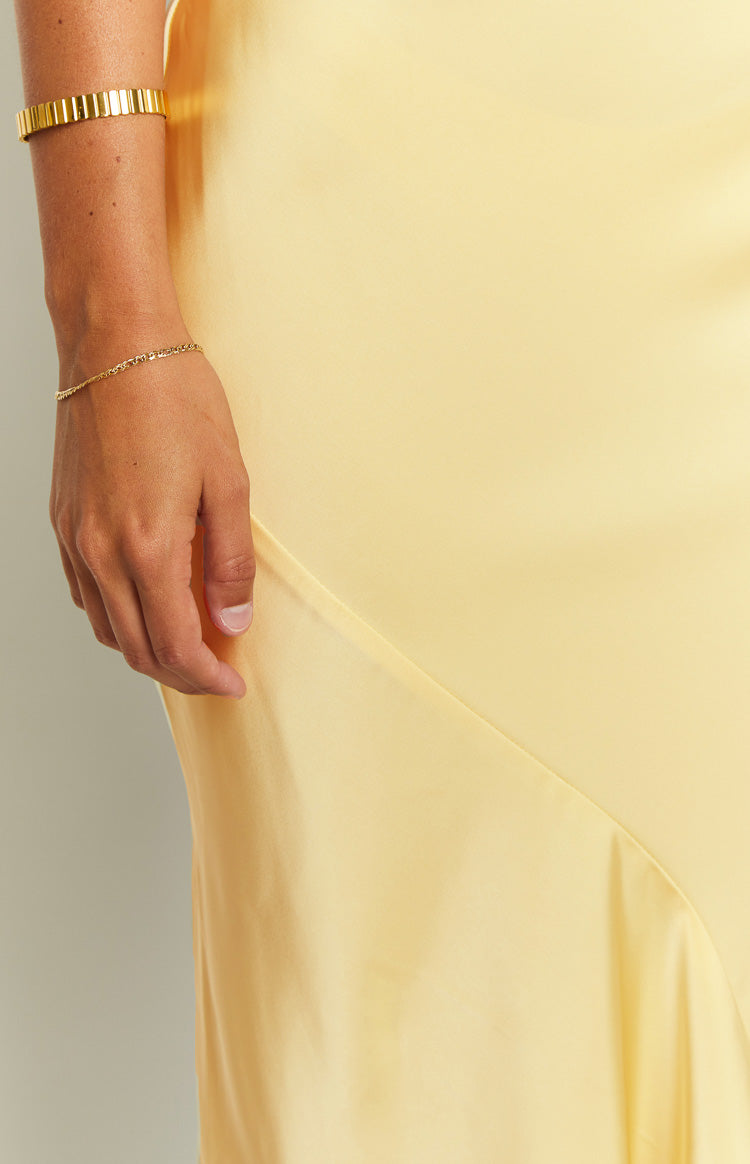 Close-up of the smooth carnation yellow satin fabric of the maxi dress