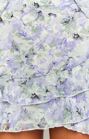 Close-up of the purple and green floral print chiffon fabric with subtle texture and tiered ruffles