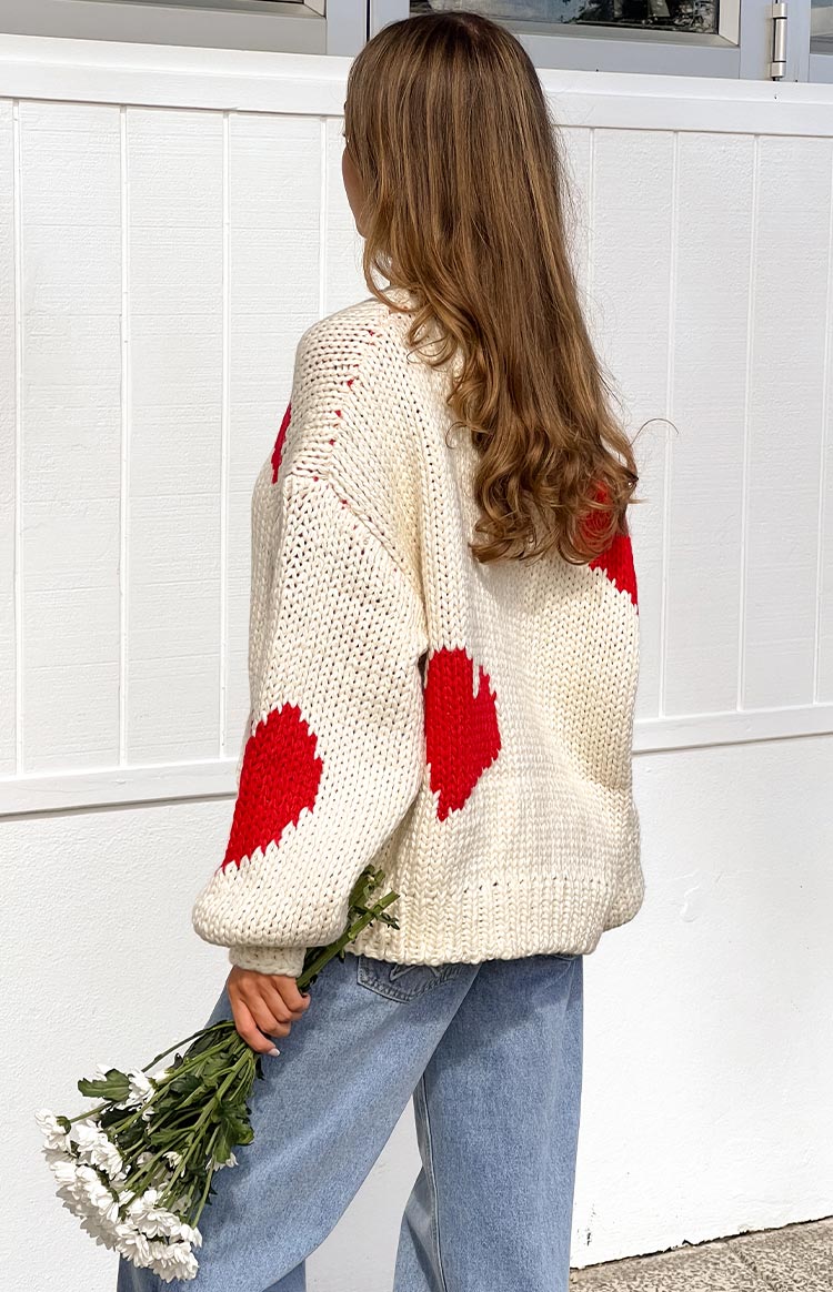 Rear and side view of a cream chunky knit sweater with red heart patterns on the back and balloon sleeves