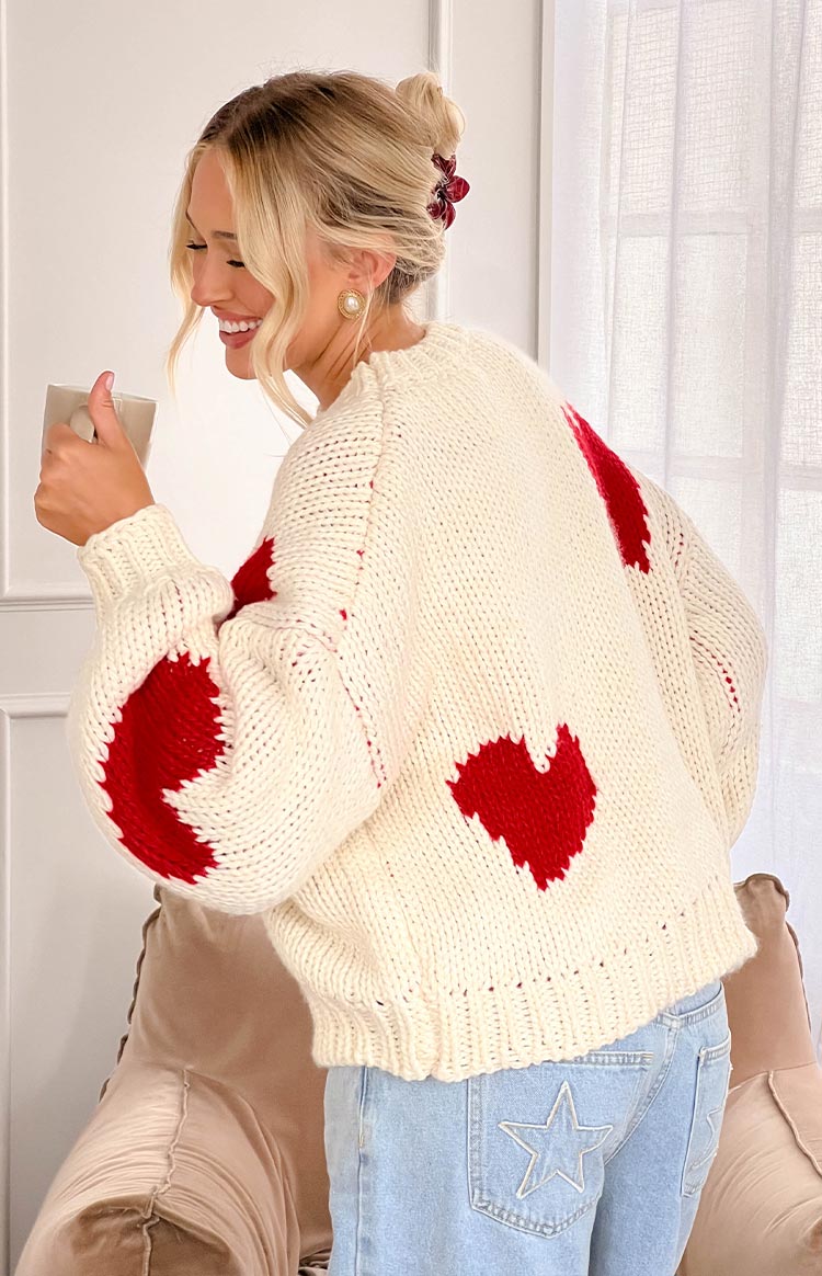 Rear view of an oversized cream chunky knit sweater with large red heart patterns on the back and puff sleeve