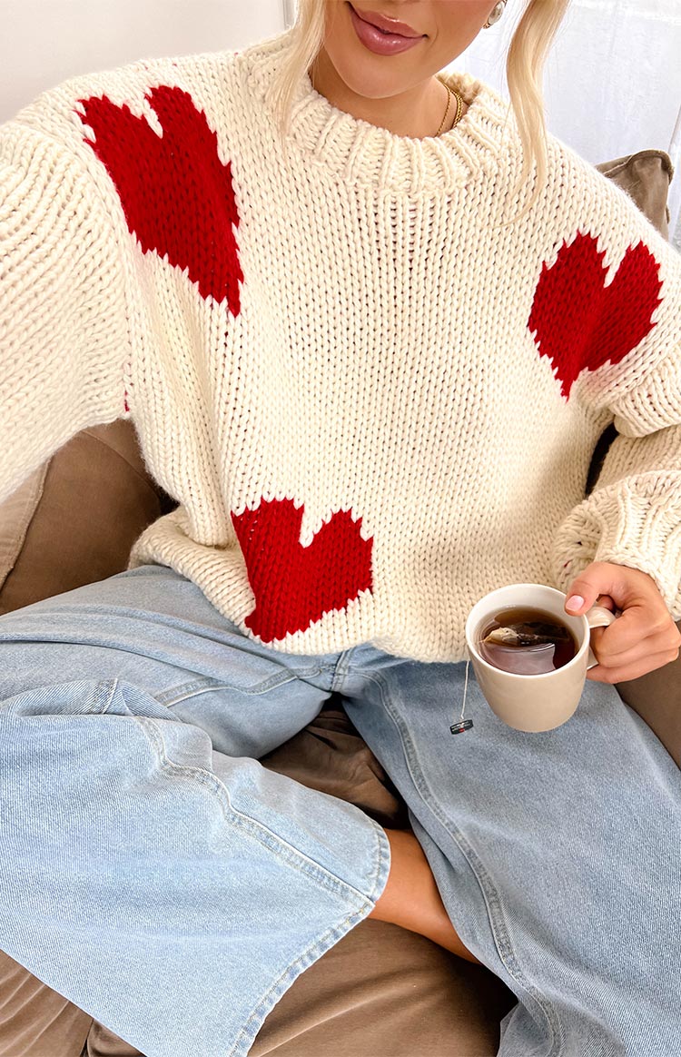 Close-up of a cream chunky knit sweater with large red heart patterns on the chest and shoulder