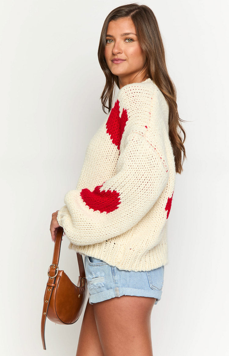 Side view of the cream chunky knit sweater with red heart patterns on the balloon sleeve and side