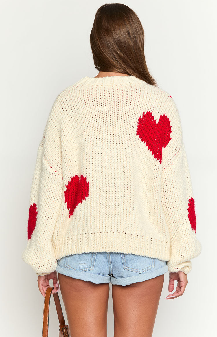 Rear view of a cream chunky knit sweater with scattered red heart patterns and ribbed hem