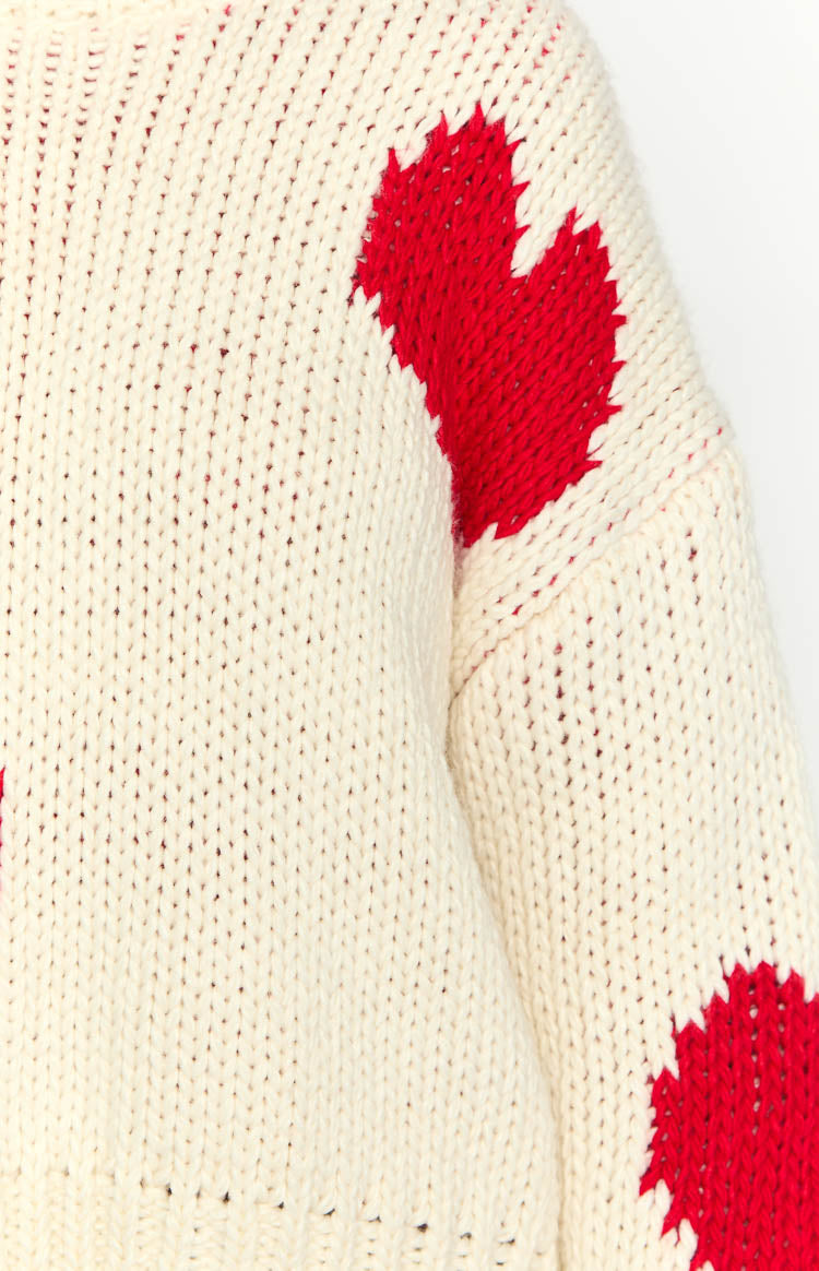 Close-up of the cream chunky knit sweater fabric with a large red heart pattern on the shoulder