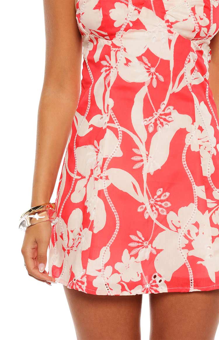 Close-up of the red floral mini dress side panel with white eyelet embroidery and cut-out hem