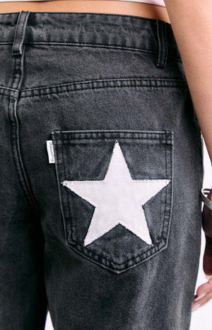 An extreme close-up of a back pocket on dark wash denim jeans highlighting a large stitched white star applique.