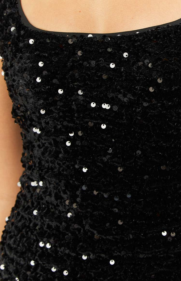 Close-up of the black sequin mini dress fabric, showing the small round sequins, textured base, and neckline binding