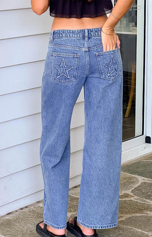 model wearing mid wash low rise denim jeans with star patch details on the back pockets