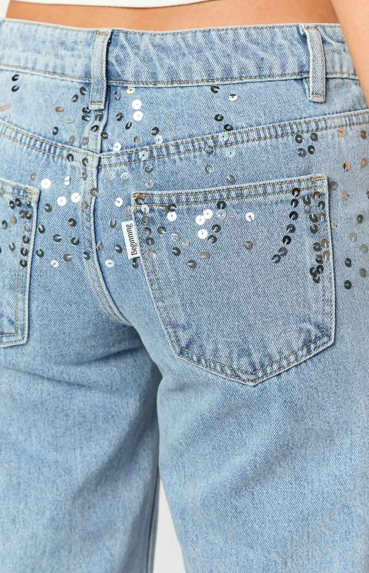 Back view close-up of light wash denim jeans with scattered silver sequins on the upper back and back pockets