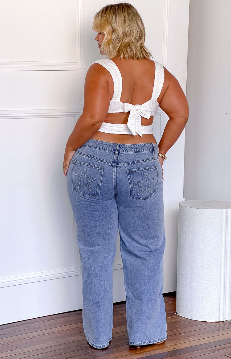 Rear view of mid wash denim low rise jeans with star embroidery on the back pockets and a wide leg fit
