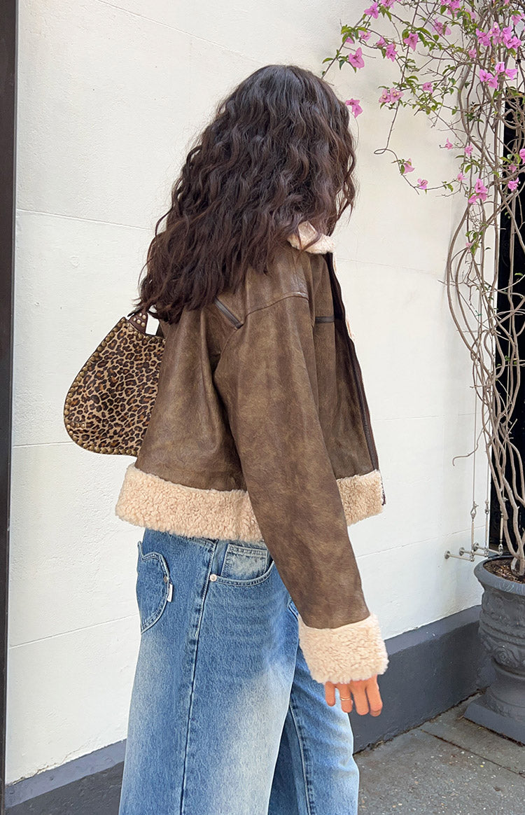 Side view of a distressed brown aviator jacket with cream sherpa lining at the cropped hem and cuffs