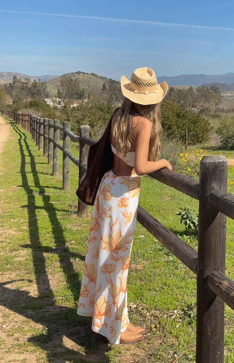 Rear view of an orange floral strapless maxi dress with waist cutouts and a flowy skirt