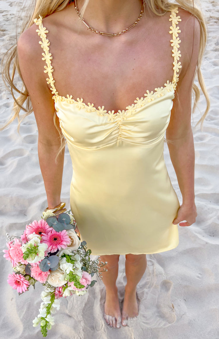 Close-up of the yellow satin mini dress showing flower detail spaghetti straps and a ruched bust