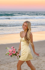 Profile view of a yellow satin mini dress, showing the ruched bust and floral spaghetti straps
