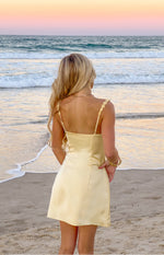 Rear view of a yellow satin mini dress with a straight back and delicate flower details on the spaghetti straps