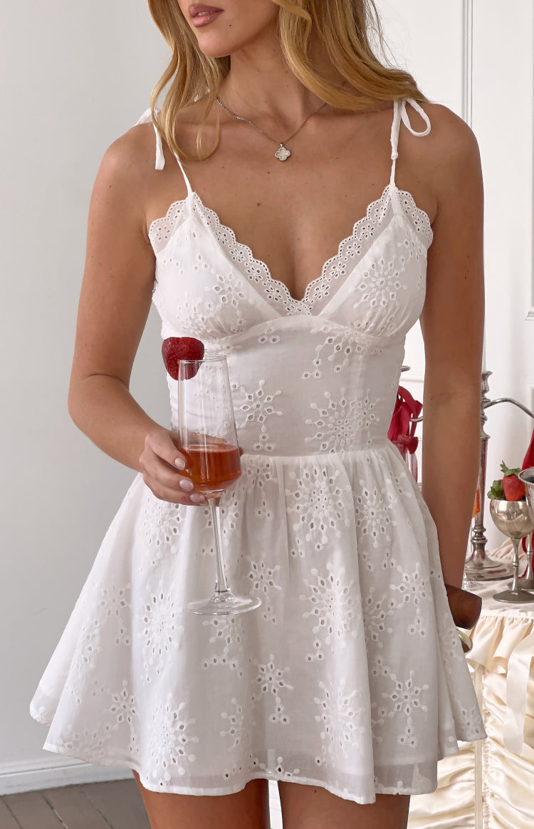 White cotton broderie mini dress with a scalloped V-neck, tie-shoulder straps, and floral cutout details